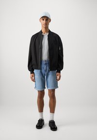 Svart bomberjakke, grå t-skjorte, lyseblå denimshorts, svarte joggesko, hvite sokker, lyseblå caps. Enkelt urbant antrekk.