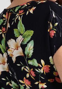 Květinová blůza s tmavě námořnickým pozadím, velkými hibisky a zelenými listy, zakončená malým otvorem na zadním krku.