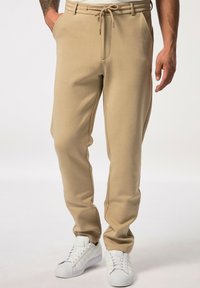 Beige Sweatpants mit schmalem Schnitt, Kordelzugbund und Seitentaschen, kombiniert mit weißen Sneakern. Weicher Stoff mit leichter Textur.
