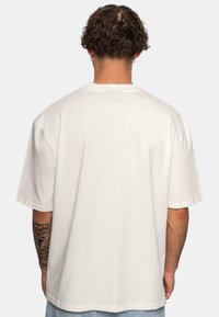 Tricou alb din bumbac cu o croială relaxată, mâneci scurte și decolteu rotund. Prezintă un design simplu pe spate, fără grafice sau accente suplimentare.