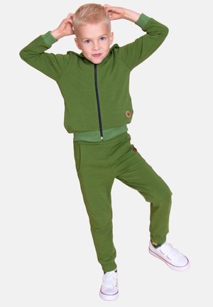 Zielony dres bawełniany z bluzą na zamek z kontrastującym suwakiem oraz spodnie dresowe ze ściągaczami. Całość dopełniają białe sneakersy.