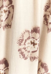 Měkká tkanina s béžovým pozadím a abstraktními květinovými vzory v tlumených odstínech mauve a hnědé, která předvádí texturovaný povrch.