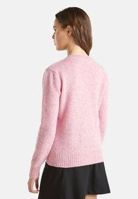 Růžový pletený svetr s kulatým výstřihem, dlouhými rukávy a vroubkovaným lemem. Jemná textura s mírně chlupatým vzhledem.