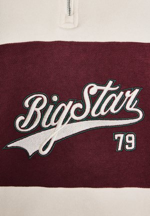 Pulover s četrtinskim zadrgo v kremni in burgundski barvi, ki prikazuje nebežno "Big Star" v belih vezenih črkah s zelenim obrobjem in številko "79".