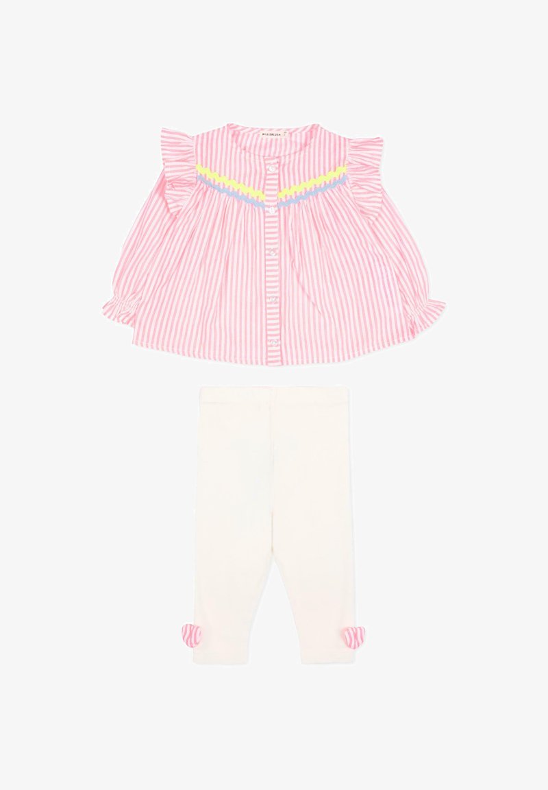 Blouse à manches longues rayée rose et blanche avec volants et bordure jaune-bleu, associée à des leggings blancs ornés de nœuds rayés roses au niveau des chevilles.