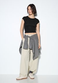 Sort cropped t-shirt, cremefarvede vidde bukser og en sort-hvidternet skjorte med knude. Beige sneakers med brun sål.