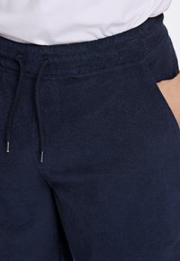 Marinblå sweatpants i mjukt tyg med elastisk midja, detaljer med dragsko och sidofickor. Slät textur, avslappnad design.
