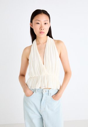 Lichte crème, mouwloze haltertop met een diepe halslijn en geraffineerde taille. G gecombineerd met lichtblauwe high-waisted jeans, met een gladde stoftextuur.