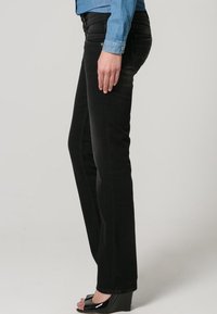 Jeans rectos negros de mezclilla, con detalles de costura sutil y diseño de cinco bolsillos, combinados con una camisa de mezclilla azul y sandalias de cuña negras.