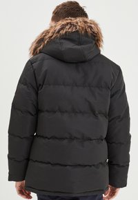 Giacca nera gonfiabile con cappuccio removibile, con una finitura in pelliccia sintetica al colletto, texture trapuntata e cuciture orizzontali.