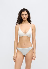 Σουτιέν σε ανοιχτό μπεζ χρώμα με βαθύ V ντεκολτέ και λεπτές τιράντες, συνδυασμένο με ανοιχτό μπλε ημιδιάφανο ριγέ εσώρουχο, με λείο ύφασμα και μίνιμαλ σχεδιασμό.