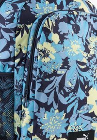 Rucksack mit Blumenmuster in Blau und Gelb auf dunklem Hintergrund, vorderer Reißverschlussfach und seitlichem Netzfach.