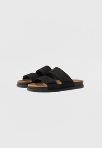 Black suede slide sandals featuring two wide straps and a cushioned insole, with a flat rubber sole and a natural texture.