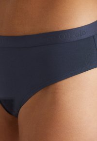 Marinblå damunderkläder i mjukt, elastiskt material, med en matt midja som har en diskret logotyp och släta, sömlösa kanter.