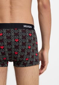 Sorte bokserbriefs med "HUG" og hjerte-mønstre i rødt og hvidt. Elastisk linning med "HUGO"-logo, der viser en tætsiddende pasform og blødt stof.