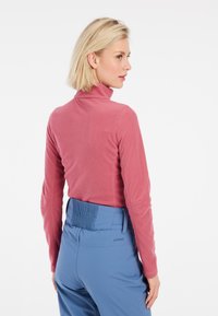 Top a maniche lunghe di colore rosa chiaro con collo alla coreana e una texture morbida, abbinato a pantaloni blu con vita arricciata e marchio.