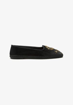 Scarpa nera piatta slip-on con perline dorate e decorazioni di gioielli sulla punta arrotondata e dettagli cuciti sulla suola.