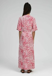 Robe maxi blanche avec un motif éclaboussé rouge, manches courtes évasées, taille élastique et jupe fluide.