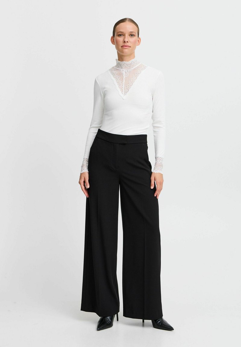 Hvid langærmet bluse med blonde detaljer ved halsudskæringen, parret med sorte bukser med bred ben. Sættet har et elegant, moderne design.