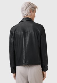 Zwarte leren jas met een klassiek ontwerp, voorzien van een spreidkraag, lange mouwen en een gladde textuur. Eenvoudig stiksel op de achterkant.