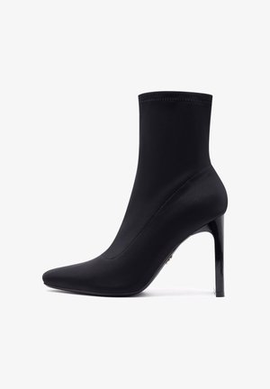 Zwarte enkelboot van gladde stof met een slanke, puntige neus en een hoge, glanzende hak. Naadloos ontwerp met subtiele stikdetails.