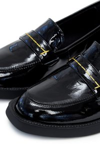 Mocassins en cuir verni noir avec une finition lisse, des accents de couture jaunes et un bout arrondi. La semelle est plate et texturée.