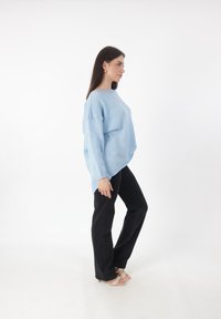 Suéter extragrande de color azul claro con mangas largas, puños acanalados y dobladillo curvado. Combinado con pantalones negros de campana y tacones de tiras beige.