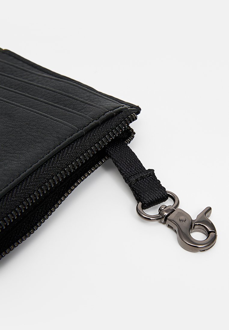 Funda con cremallera negra de cuero sintético texturizado, diseño plano y un tirador de cremallera de tela negra con un clip de metal para sujeción.