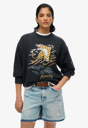 Black sweatshirt with embroidered tiger design, oversized fit, round neckline, and ribbed cuffs. Paired with light blue denim shorts.