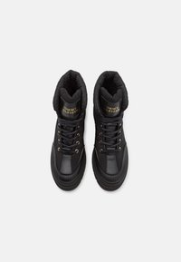 Baskets montantes noires Tommy Hilfiger avec des cols matelassés, œillets dorés et lacets, vues de dessus sur un fond blanc.