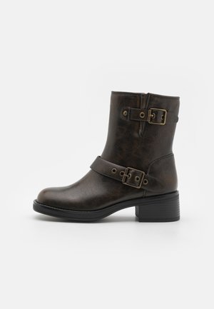 Brown leather ankle boot with two decorative buckles, round toe, and a low block heel. Textured finish with a rugged appearance.