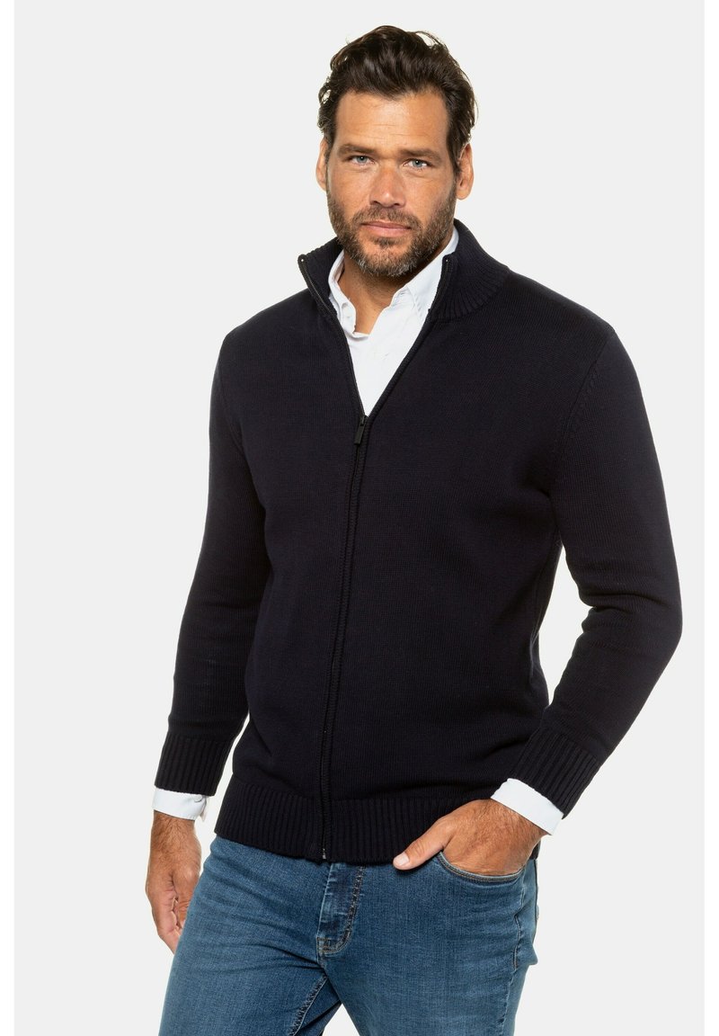 Mörkblå zip-up tröja i stickad tyg med ribbat krage och manschetter, med en frontdragkedja och en figurnära design. Bärs över en vit skjorta.