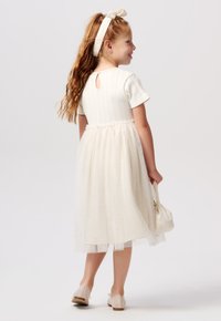 Witte jurk met korte geribde mouwen, een tule rok en een sleutelgatdetail op de rug. Inclusief een bijpassende hoofdband en beige schoenen.