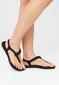 Black flip-flop sandals with a textured sole, featuring a flat, flexible strap design and adjustable buckle for secure fit.