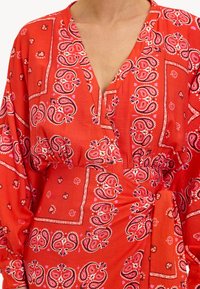 Vestido rojo con estampado de cachemira, con escote en V, mangas largas, cintura elástica y un detalle atado en un lado. Fabricado en una tela ligera.