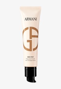 Beige tube med en glatt overflate, med en svart pumpe og brun logo. Teksten sier "SKIN TINT long-wear & care." Glatt overflate, kompakt form.