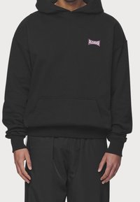 Felpa nera con cappuccio e tasca frontale, con polsini a coste. Presenta un piccolo logo viola "PEGADOR" sul lato sinistro del petto. Tessuto morbido.