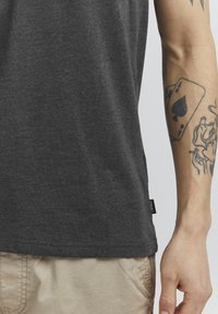 T-shirt à manches courtes gris foncé en tissu doux avec un ourlet droit, associé à un pantalon clair, comportant une étiquette sur le côté.