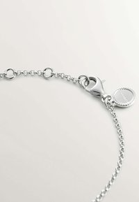 Pulsera de cadena de plata con eslabones circulares, un cierre de langosta y un charm redondo con un patrón en relieve. Superficie metálica suave, diseño minimalista.