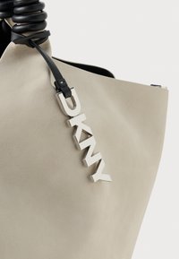 Lichtbeige leren tas met zwarte gekrulde handgreep en een zilverkleurige "DKNY" charme die aan een dunne zwarte strap hangt.