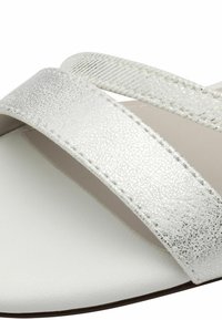 Bijele sandale s dvije široke trake; jedna glatke, sjajne završne obrade, a druga s teksturiranim, metalnim izgledom. Fleksibilna potplat, minimalistički dizajn.