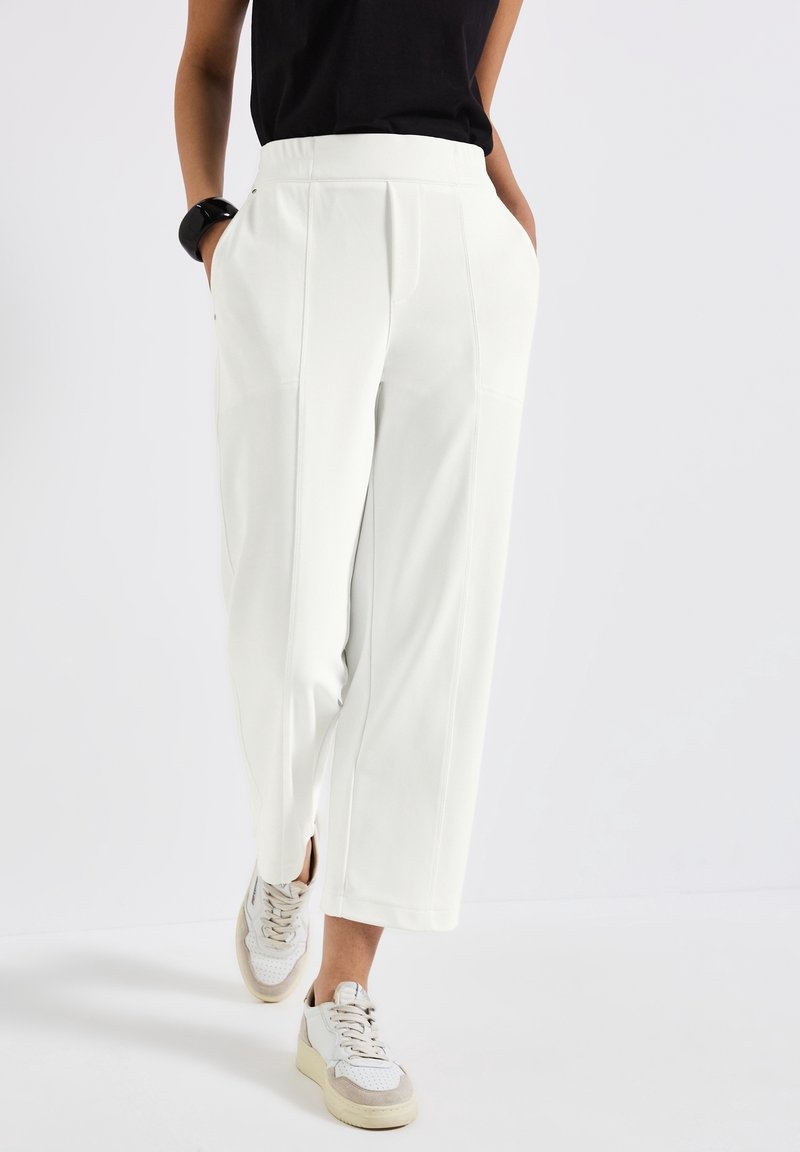 Vita skräddarsydda byxor med bred bendesign, med sidofickor och synliga sömdetaljer, exklusivt kombinerade med ljusfärgade sneakers.