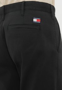 Μαύρο βαμβακερό παντελόνι με πίσω τσέπη και λογότυπο «TOMMY JEANS» σε κόκκινο, λευκό και μπλε. Απαλή υφή, κομμένη εφαρμογή.