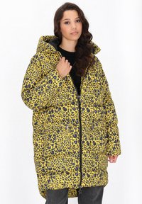 Gul puffjacka med svart leopardmönster, med huva, framsidans dragkedja och sidofickor. Tjock, quiltad textur.