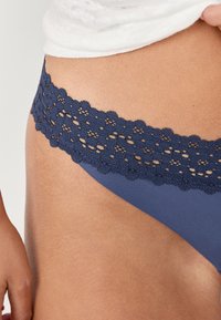 String navy bleu avec une ceinture en dentelle décorative ornée de motifs floraux, texture de tissu douce et finition lisse.