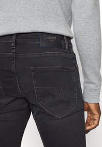 Jeans de mezclilla negra con una textura suave, que presentan una etiqueta de JOOP! en la cinturilla y costuras en contraste. Los bolsillos traseros tienen un diseño único en forma de V.