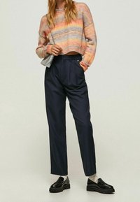 Pull en tricot multicolore avec des rayures horizontales dans des tons pastel, associé à un pantalon taille haute bleu marine et des mocassins noirs. Détails de tissu texturé.