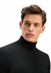 Schwarzer Rollkragenpullover aus geripptem Strickstoff, mit taillierter Passform und hohem Kragen, präsentiert vor einem schlichten weißen Hintergrund.