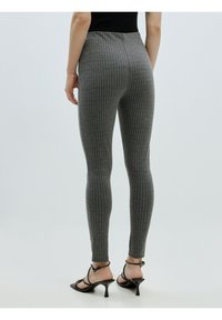 Grijze pinstripe legging gemaakt van zachte stof, met een aansluitend ontwerp en een enkellange snit. Draagt met zwarte hakken sandalen.