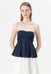 Strapless navy top in ribbed texture, featuring a fitted bodice and flared peplum hem. Smooth fabric with a subtle sheen.